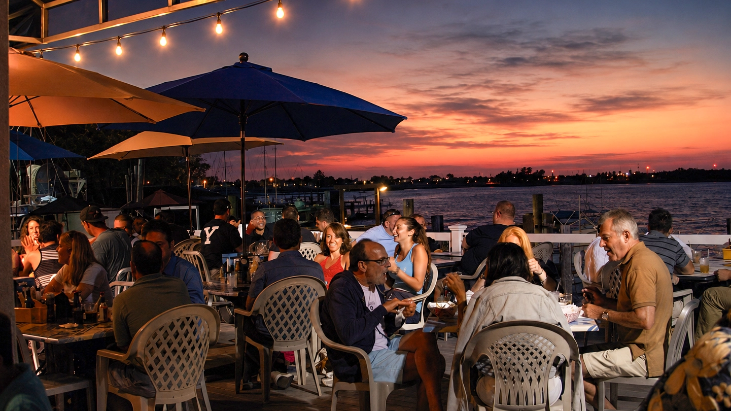 Guests dining at The Buoy Bar as string lights come on over Reynolds Channel
